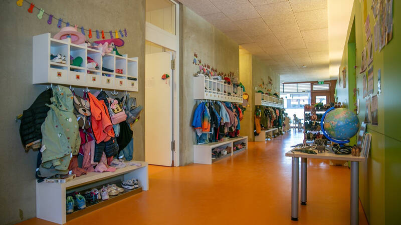 Ein farbenfroher Kindergartenflur mit Kinderkleidung, Schuhen und einem Tisch mit einem Globus und Spielzeug.