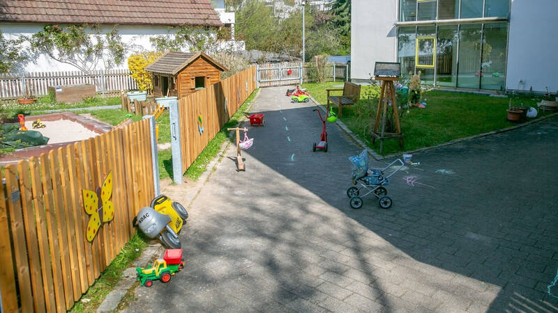 Ein Spielplatz mit Spielzeug und einem Holzspielhaus, umgeben von einem Holzzaun mit bunten Dekorationen.