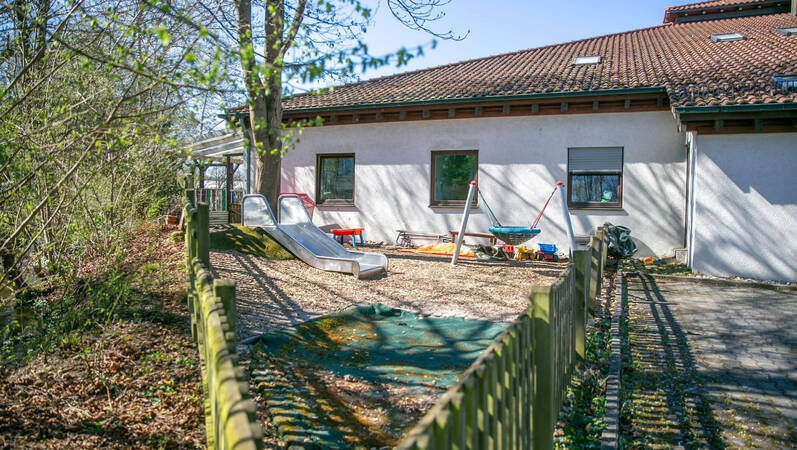 Ein kleiner Spielplatz mit einer Rutsche und einer Schaukel befindet sich neben einem weißen Gebäude mit Ziegeldach.
